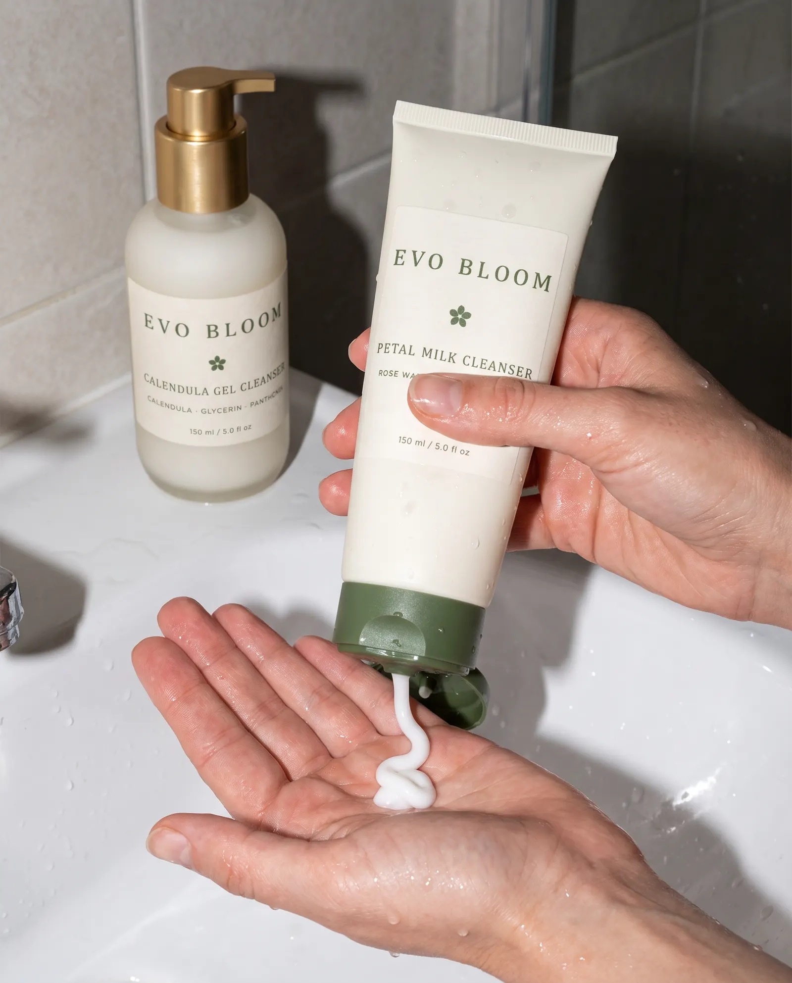 Petal Milk Cleanser squeezed into a wet palm at a basin, with Calendula Gel Cleanser on the edge